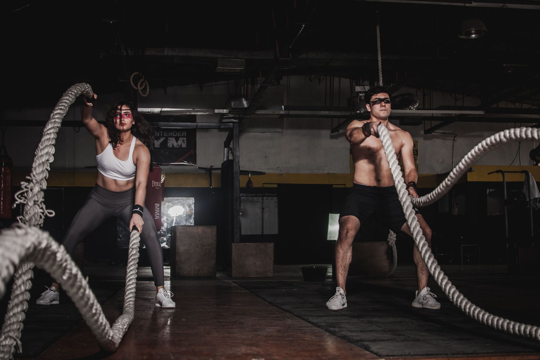 Two athletes working battle ropes in a dark gym
