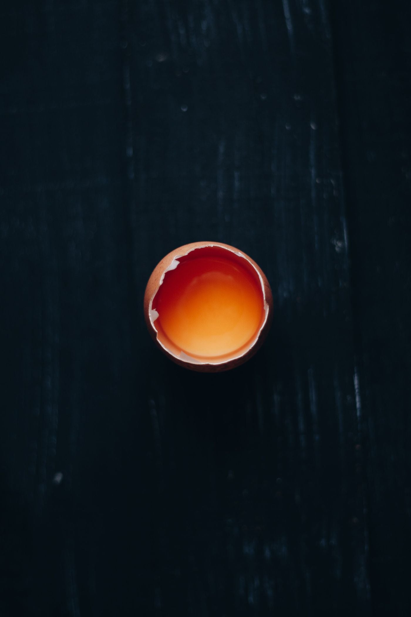 A cracked egg half, yolk intact and glowing, on a near-black surface